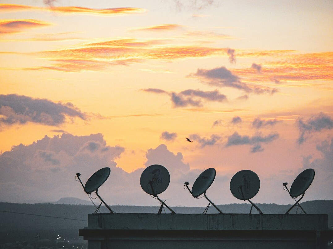 Satellite uplink dish transmitting a live broadcast signal against the sky