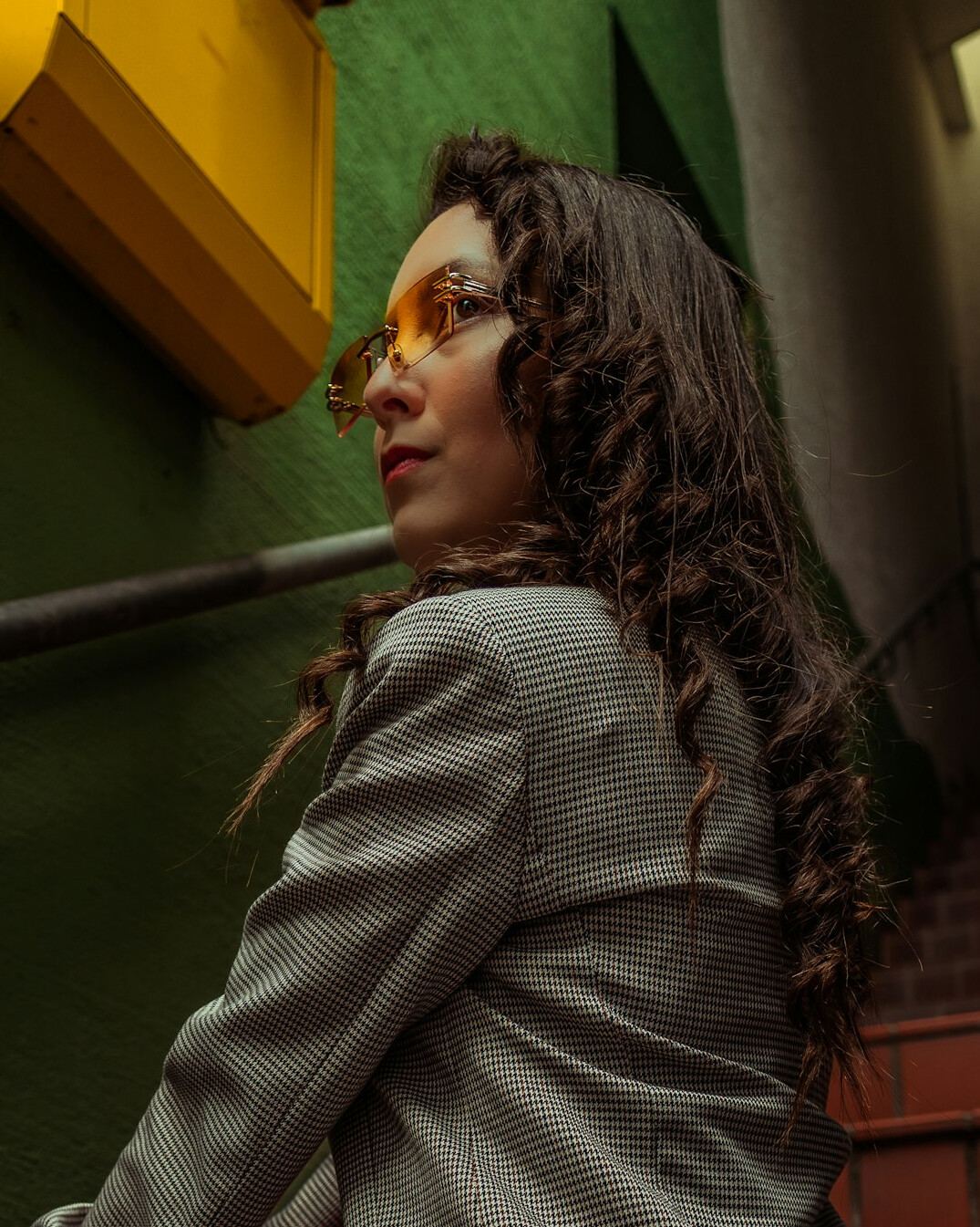 Studio portrait of a woman with curly hair wearing glasses and a blazer